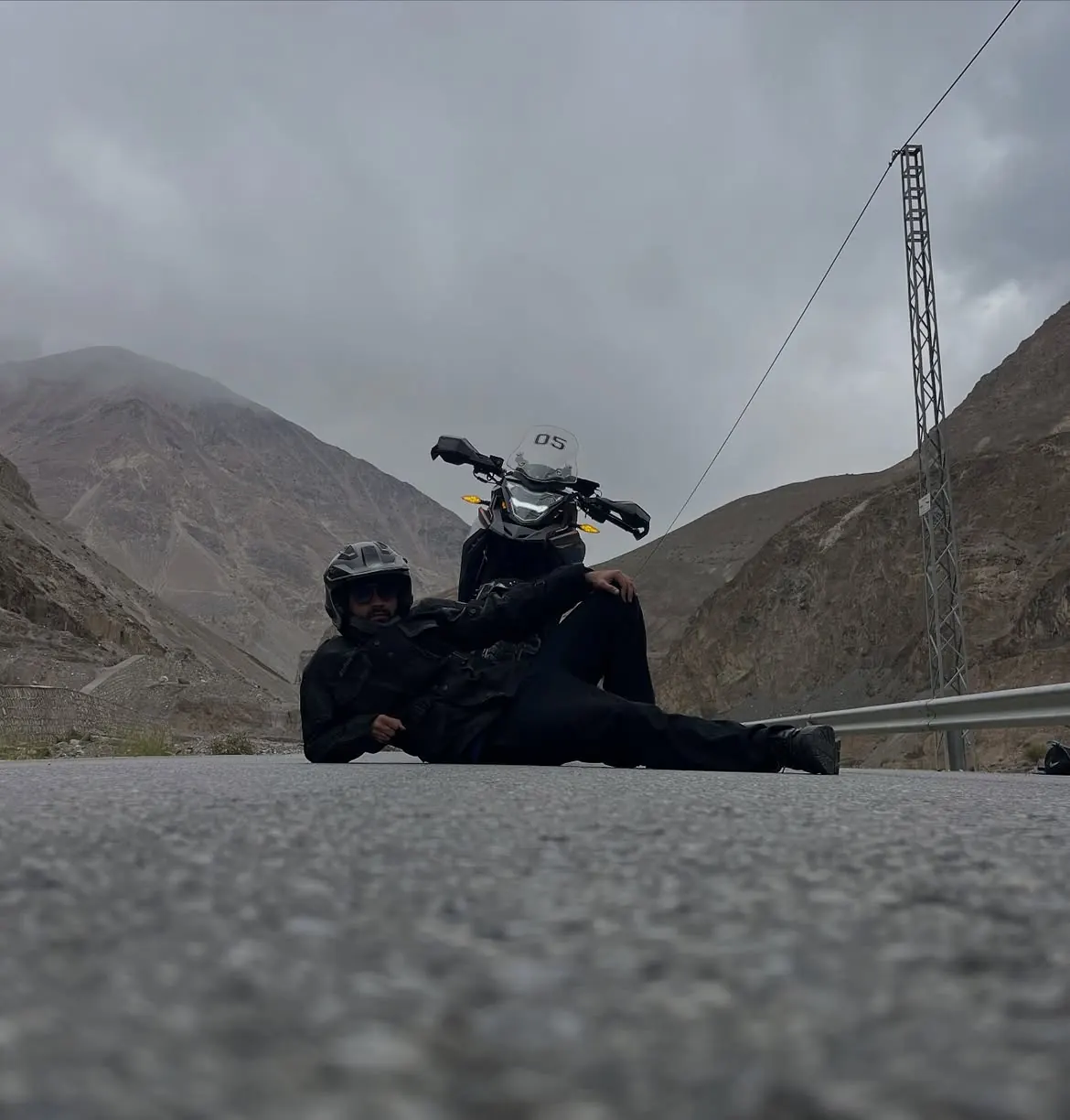 Motorcycle rider resting on a mountain road beside an adventure bike
