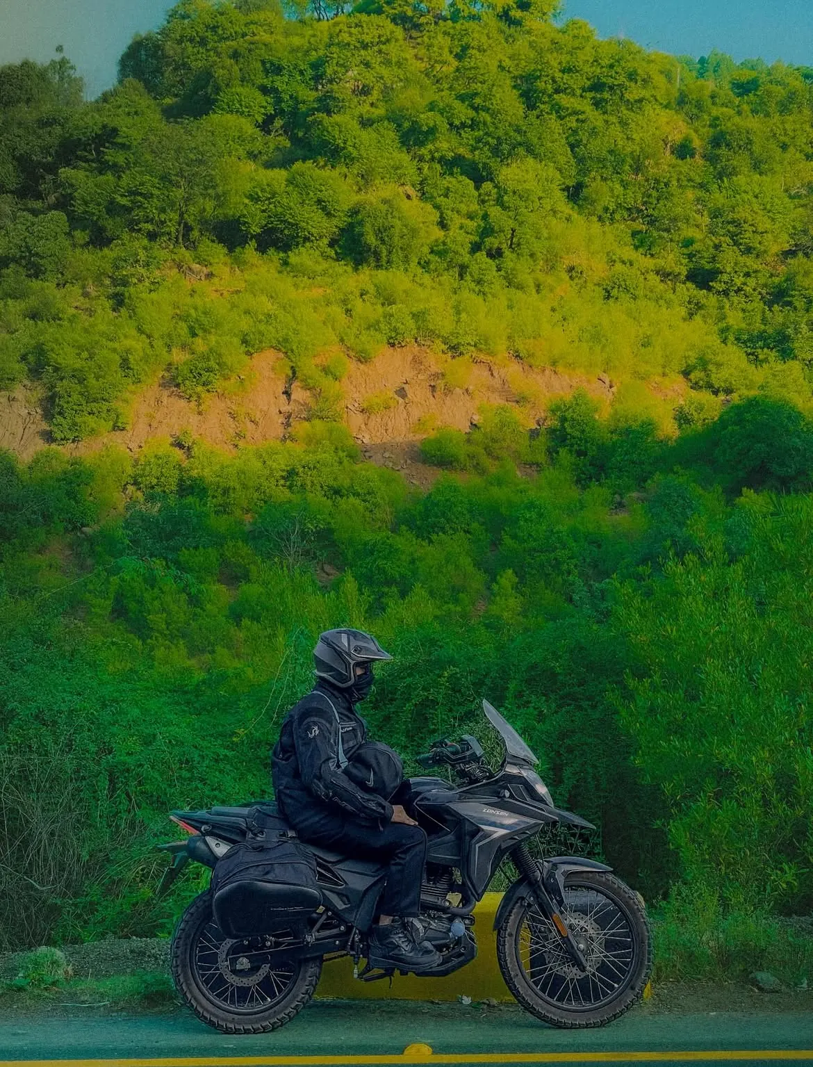 Motorcycle rider beside a green hillside road in Pakistan